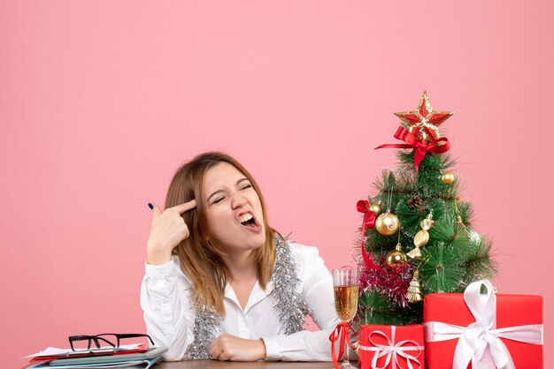 Vorderansicht der Arbeiterin, die hinter ihrem Tisch mit Geschenken auf rosa sitzt