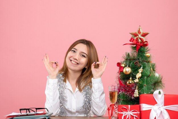 Vorderansicht der Arbeiterin, die hinter ihrem Tisch mit Geschenken auf rosa sitzt