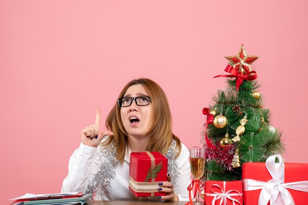 Vorderansicht der Arbeiterin, die mit Weihnachtsgeschenken auf rosa sitzt