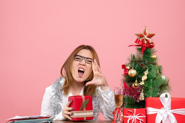 Vorderansicht der Arbeiterin, die mit Weihnachtsgeschenken auf rosa sitzt