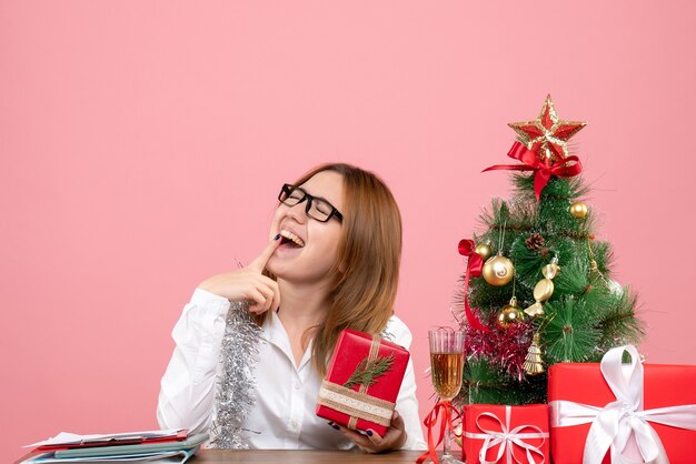 Vorderansicht der Arbeiterin, die mit Weihnachtsgeschenken auf rosa sitzt