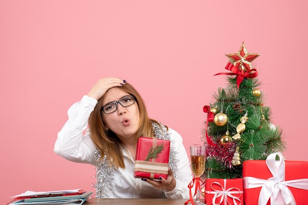 Vorderansicht der Arbeiterin, die mit Weihnachtsgeschenken auf rosa sitzt