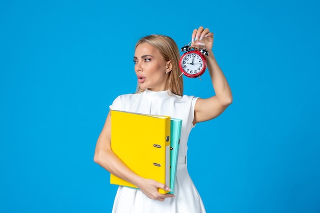 Kostenloses Foto vorderansicht der arbeiterin, die ordner und uhr an blauer wand hält