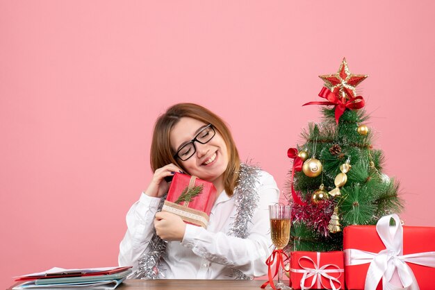 Vorderansicht der Arbeiterin, die um Weihnachtsgeschenke und Baum auf rosa sitzt