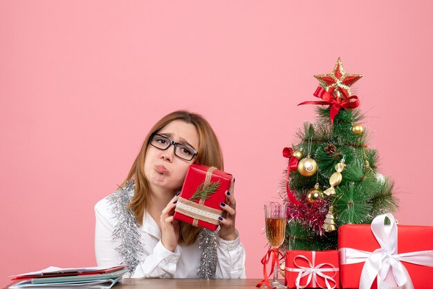 Vorderansicht der Arbeiterin, die um Weihnachtsgeschenke und Baum auf rosa sitzt