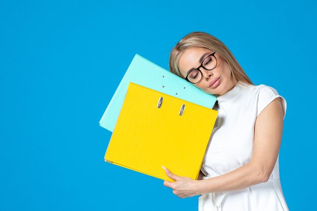 Vorderansicht der Arbeiterin im weißen Kleid, die verschiedene Ordner an der blauen Wand hält