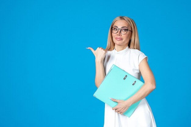 Vorderansicht der Arbeiterin im weißen Kleid mit blauem Ordner an blauer Wand