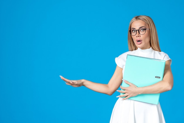 Vorderansicht der Arbeiterin im weißen Kleid mit blauem Ordner an blauer Wand