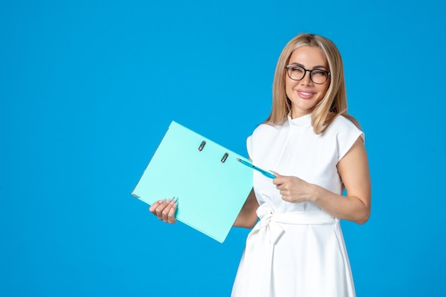 Vorderansicht der Arbeiterin im weißen Kleid mit blauem Ordner an blauer Wand