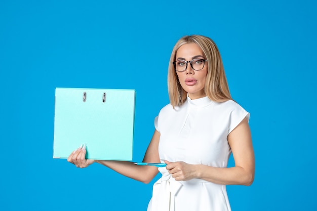 Vorderansicht der Arbeiterin im weißen Kleid mit blauem Ordner an blauer Wand