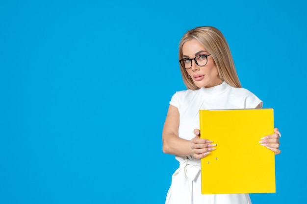 Vorderansicht der Arbeiterin im weißen Kleid mit gelbem Ordner an blauer Wand