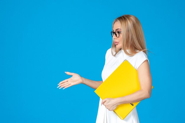 Vorderansicht der Arbeiterin im weißen Kleid mit gelbem Ordner an blauer Wand