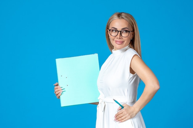 Vorderansicht der Arbeiterin im weißen Kleid mit Ordner an blauer Wand