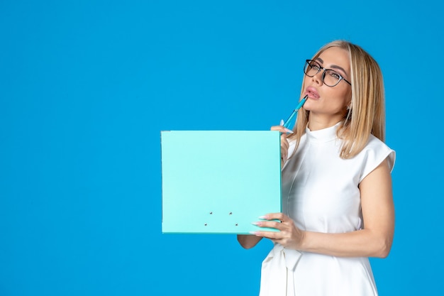 Vorderansicht der Arbeiterin im weißen Kleid mit Ordner an blauer Wand