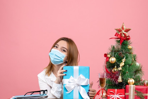 Vorderansicht der Arbeiterin in der sterilen Maske mit Geschenken auf rosa