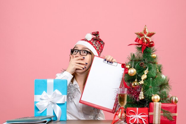 Vorderansicht der Arbeiterin sitzend und hält Aktennotiz um Geschenke mit geschocktem Gesicht auf rosa