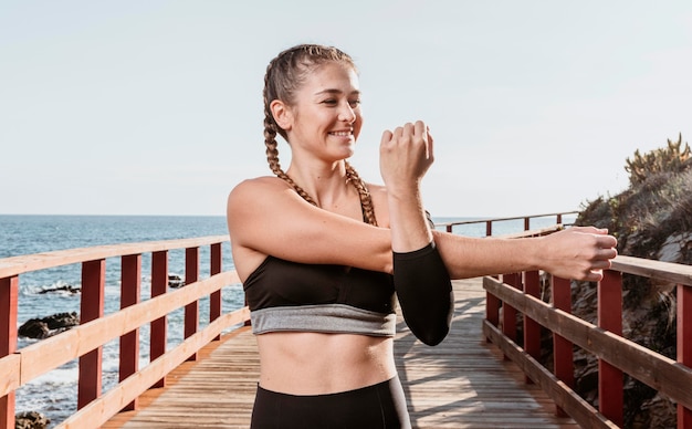 Vorderansicht der athletischen Smiley-Frau, die draußen durch den Strand streckt