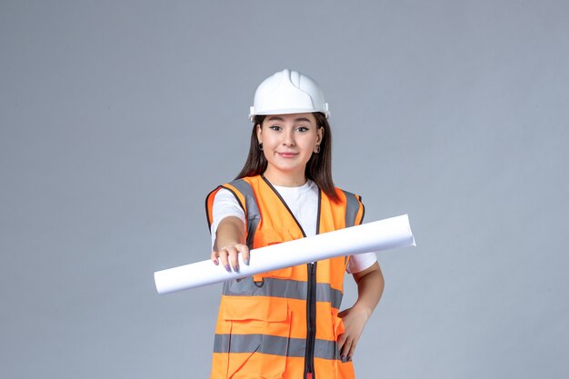 Vorderansicht der Baumeisterin in Uniform mit Poster in den Händen auf weißer Wand