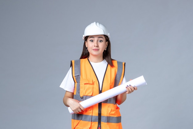 Vorderansicht der Baumeisterin in Uniform mit Poster in den Händen auf weißer Wand