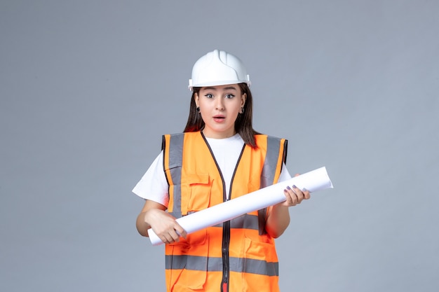 Vorderansicht der Baumeisterin in Uniform mit Poster in den Händen auf weißer Wand