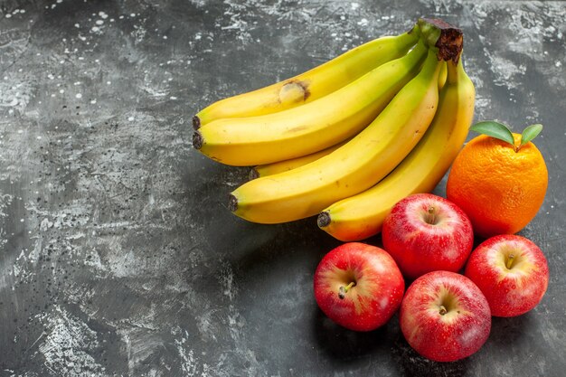 Vorderansicht der Bio-Ernährungsquelle frisches Bananenbündel und rote Äpfel und eine Orange mit Stiel auf der linken Seite auf dunklem Hintergrund