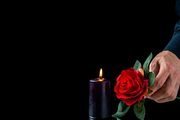 Vorderansicht der dunklen Kerze mit roter Rose und männlicher Hand auf dunkler Oberfläche