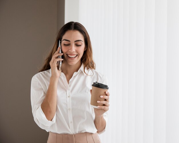 Vorderansicht der eleganten Geschäftsfrau, die am Telefon spricht, während Kaffeetasse hält