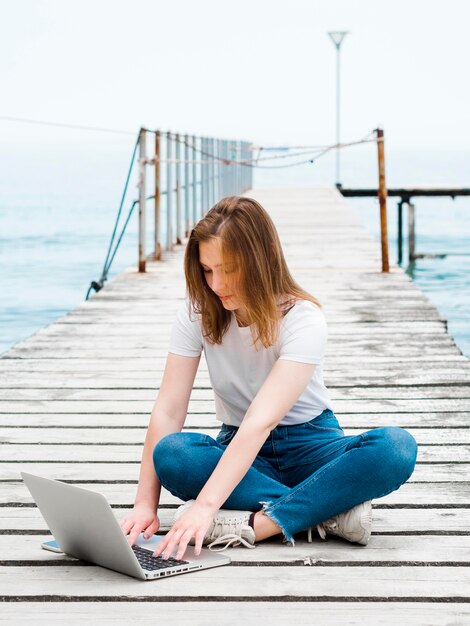 Vorderansicht der Frau, die am Laptop draußen am Pier arbeitet