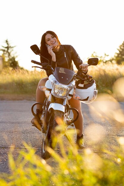 Vorderansicht der Frau, die auf Smartphone spricht, während auf ihrem Motorrad ruht