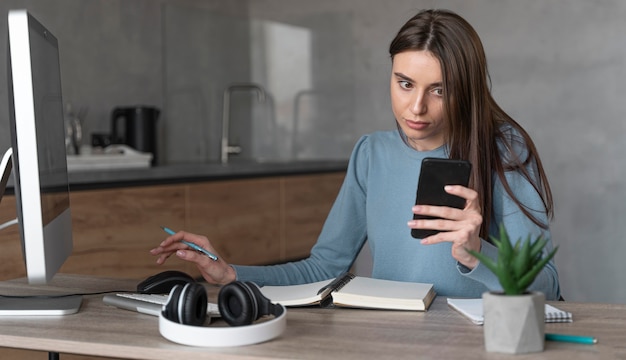 Vorderansicht der Frau, die im Medienfeld mit Computer und Smartphone arbeitet