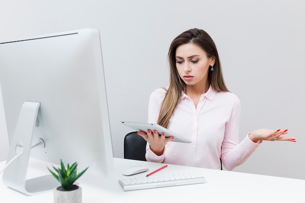 Vorderansicht der Frau, die mit ihrer Tablette beim Sitzen am Schreibtisch frustriert ist