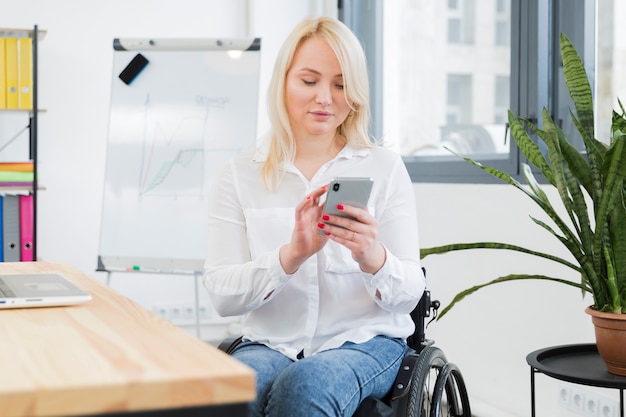 Kostenloses Foto vorderansicht der frau im rollstuhl, der smartphone hält