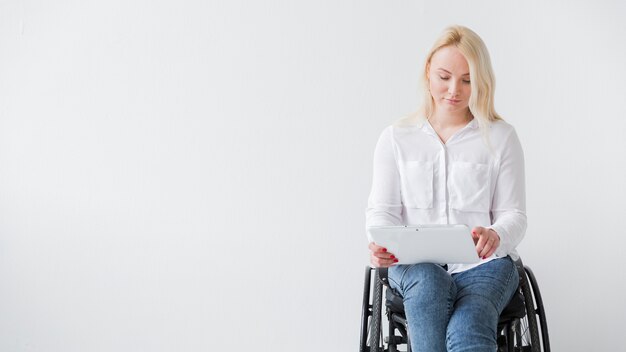 Vorderansicht der Frau im Rollstuhl, die auf Tablette arbeitet