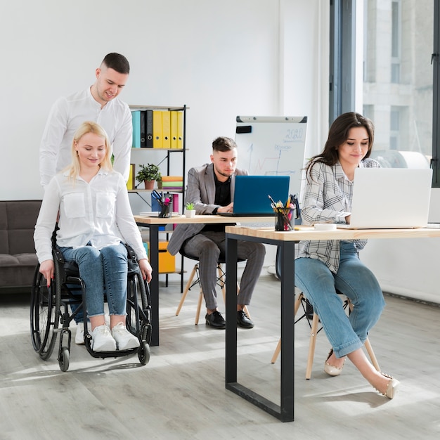 Vorderansicht der Frau im Rollstuhl, die von einem Mitarbeiter im Büro geholfen wird