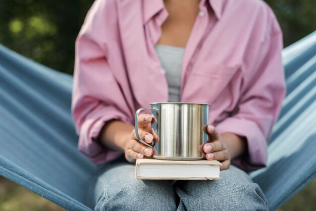 Vorderansicht der Frau in der Hängematte mit Buch und Becher