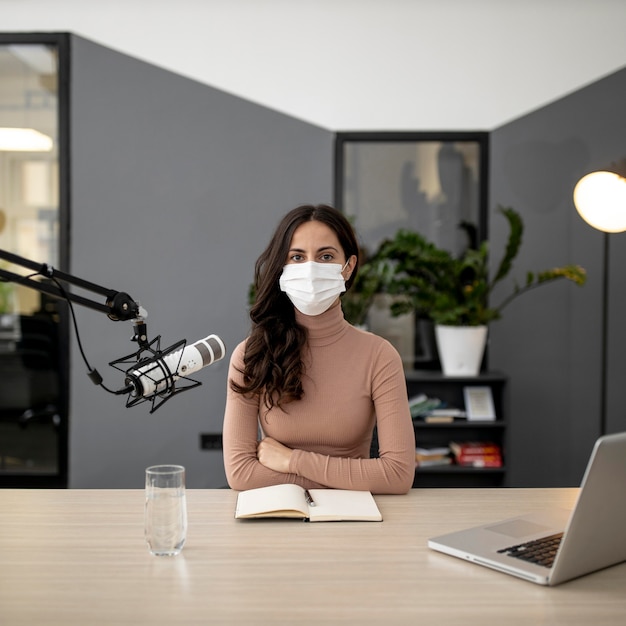 Vorderansicht der Frau mit der medizinischen Maske, die im Radio sendet