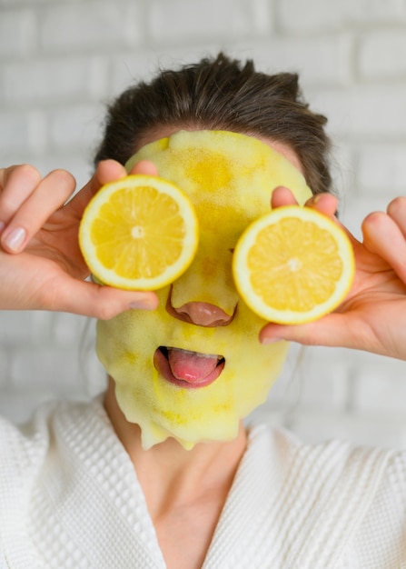 Vorderansicht der Frau mit Gesichtsmaske, die mit Zitronenscheiben aufwirft
