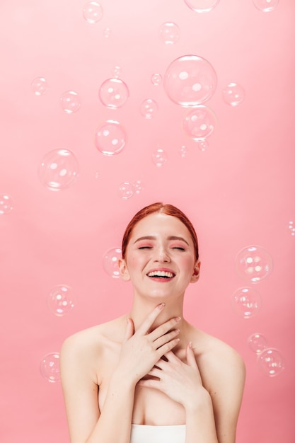 Vorderansicht der freudigen Ingwerfrau mit Seifenblasen. Atemberaubende kaukasische Mädchen lachen lokalisiert auf rosa Hintergrund.