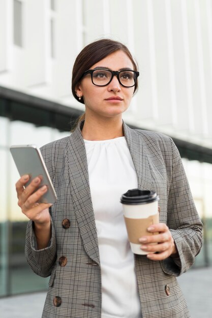 Vorderansicht der Geschäftsfrau mit Kaffee und Smartphone im Freien