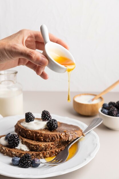 Vorderansicht der Hand, die Honig über Toast mit Blaubeeren gießt