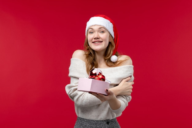 Vorderansicht der hübschen Frau mit Weihnachtsspielzeug auf Rot