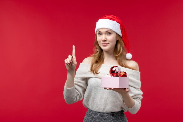 Vorderansicht der hübschen Frau mit Weihnachtsspielzeug auf Rot