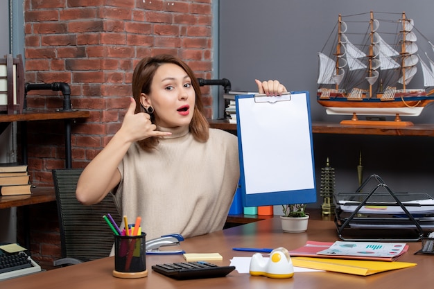 Kostenloses Foto vorderansicht der hübschen frau mit zwischenablage, die mich im büro anrufen lässt