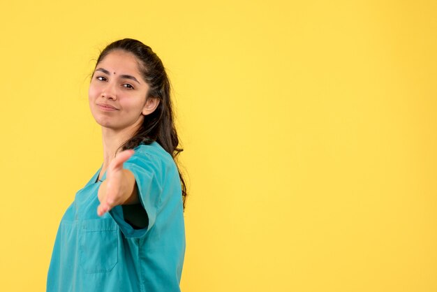 Vorderansicht der hübschen Ärztin, die Hand auf gelber Wand gibt