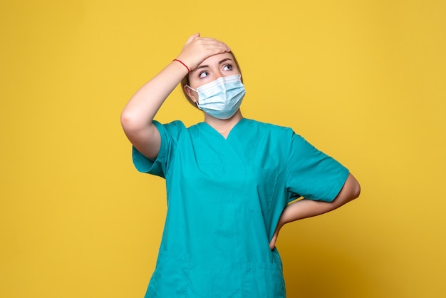 Kostenloses Foto vorderansicht der jungen ärztin im medizinischen hemd und in der sterilen maske auf gelber wand
