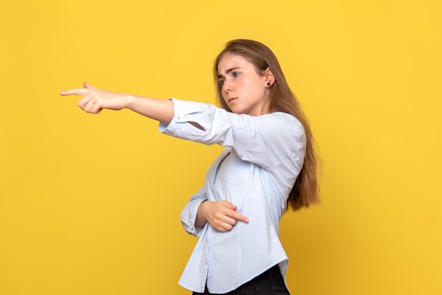 Vorderansicht der jungen Frau, die auf gelbe Wand zeigt