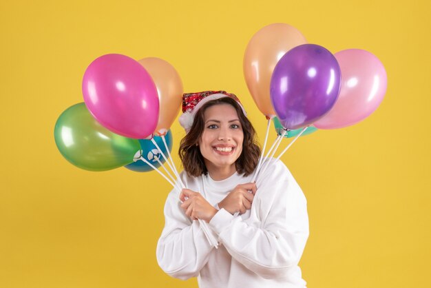 Vorderansicht der jungen Frau, die bunte Luftballons an der gelben Wand hält