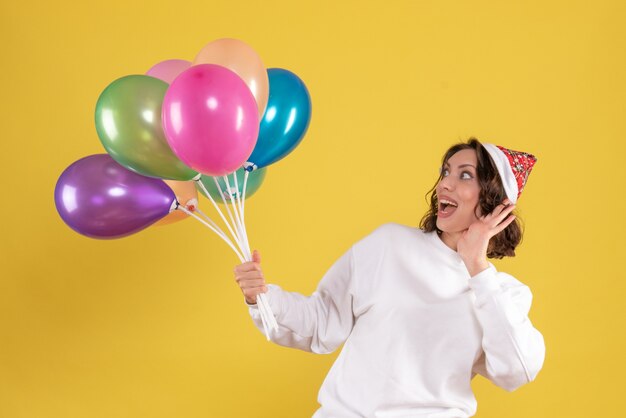 Vorderansicht der jungen Frau, die bunte Luftballons an der gelben Wand hält