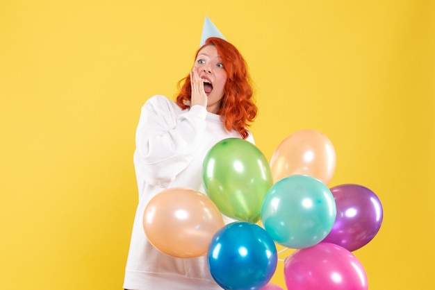 Vorderansicht der jungen Frau, die bunte Luftballons an der gelben Wand hält