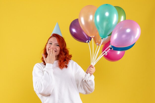 Vorderansicht der jungen Frau, die bunte Luftballons an der gelben Wand hält